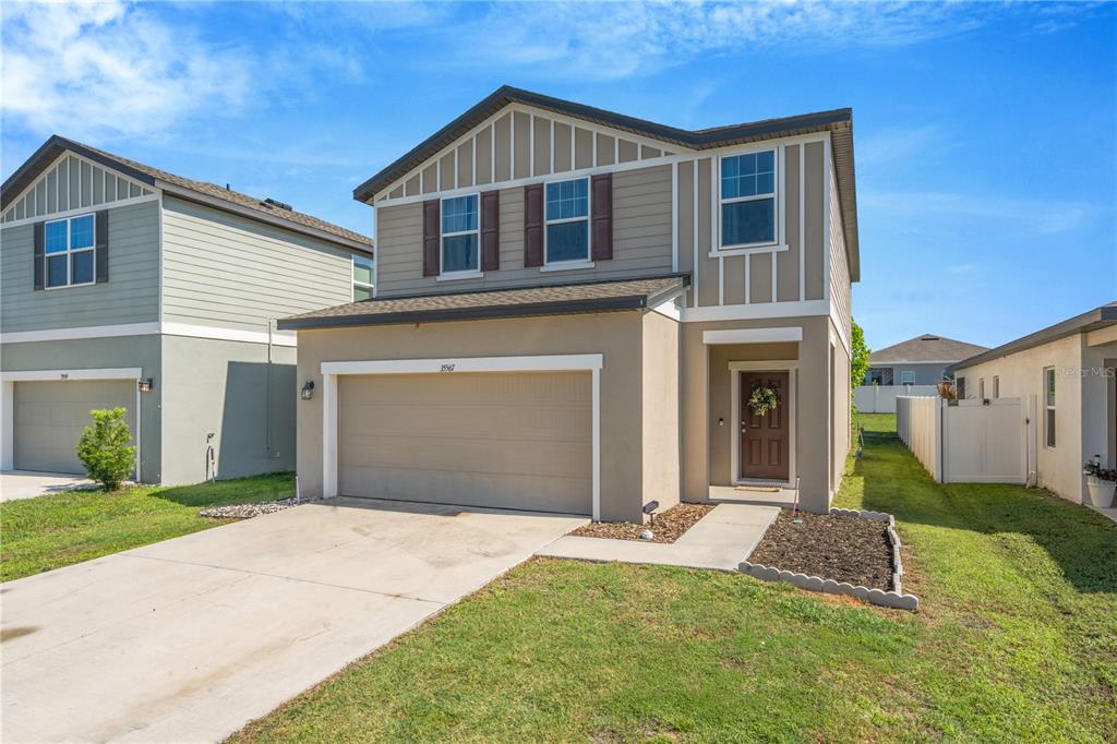 A two-story suburban house with a tan stucco exterior, a two-car garage, and brown shutters — 35567 BUTTONWEED, ZEPHYRHILLS, FL