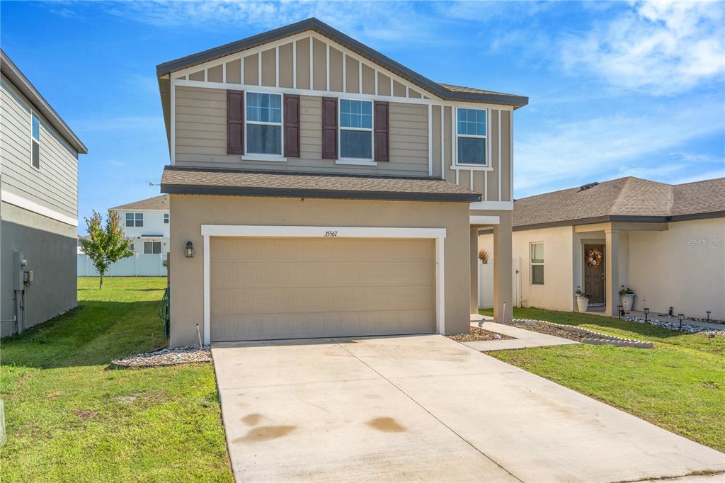 A two-story house with a tan stucco exterior, a two-car garage, and brown shutters — 35567 BUTTONWEED, ZEPHYRHILLS, FL
