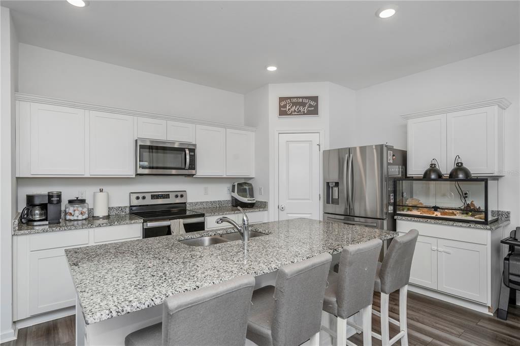 A kitchen features white cabinetry, granite countertops, a central island with seating, and stainless appliances — 35567 BUTTONWEED, ZEPHYRHILLS, FL
