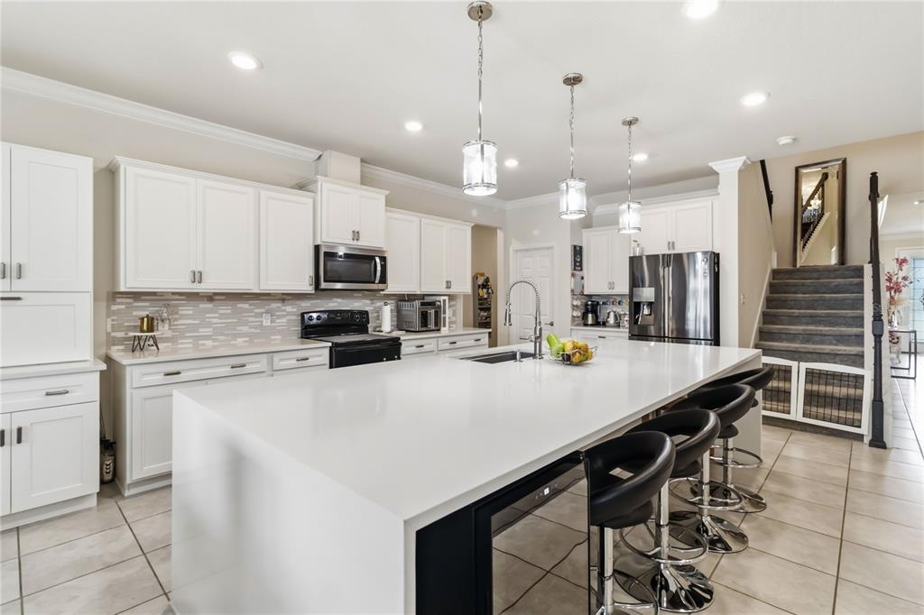 A modern kitchen features white cabinetry, a large quartz island with bar seating, and stainless appliances — 2764 MATERA DRIVE, ST CLOUD, FL