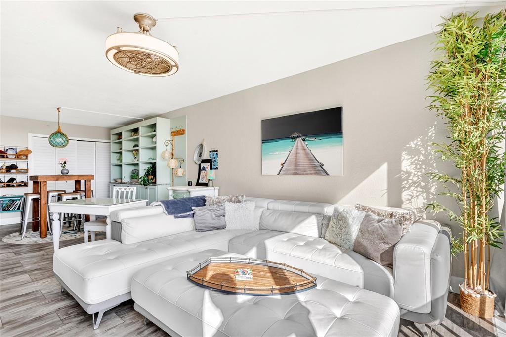 A living room features a white sectional sofa, a large ottoman, and a bamboo plant — 255 DOLPHIN POINT UNIT 407, CLEARWATER BEACH, FL