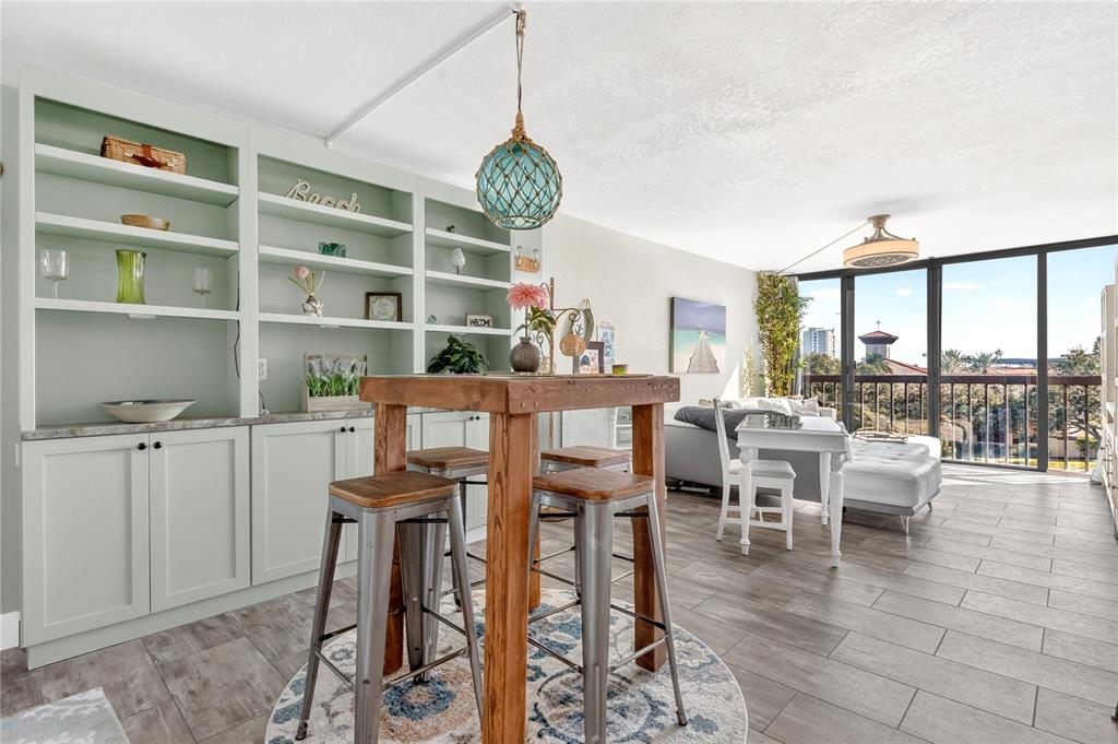 A living and dining area features light green built-in shelving, a wooden bar table, and balcony views — 255 DOLPHIN POINT UNIT 407, CLEARWATER BEACH, FL