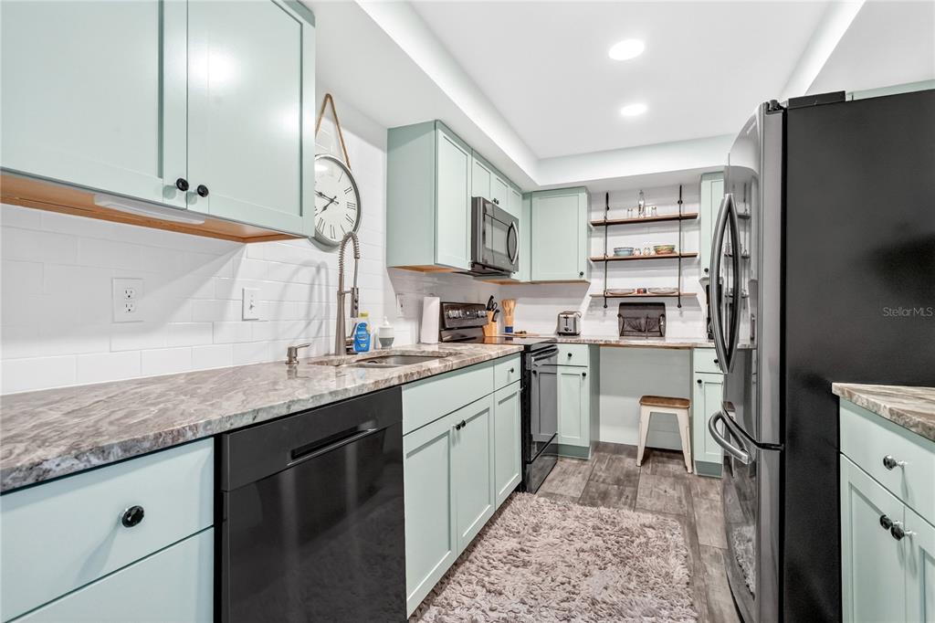 A kitchen features light green cabinets, dark countertops, black appliances, and open shelving — 255 DOLPHIN POINT UNIT 407, CLEARWATER BEACH, FL