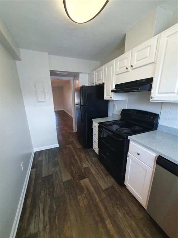 A kitchen features white cabinets, black appliances, a stainless steel dishwasher, and wood-look flooring — 1907 ORANGE BOULEVARD WAY, PALM HARBOR, FL