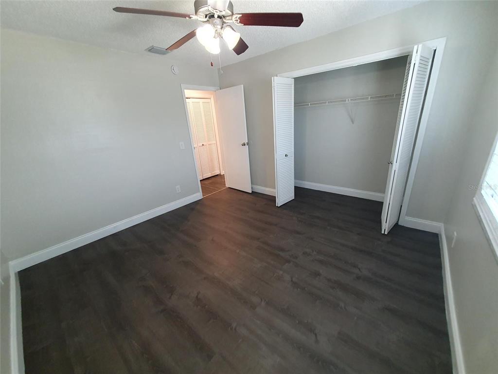 An empty living room features wood-look flooring, a ceiling fan, and sliding glass patio doors — 1907 ORANGE BOULEVARD WAY, PALM HARBOR, FL