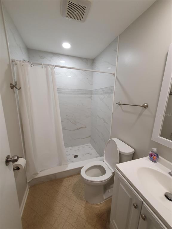 A bathroom features a walk-in shower with marble-look tile, a toilet, and a vanity — 1907 ORANGE BOULEVARD WAY, PALM HARBOR, FL