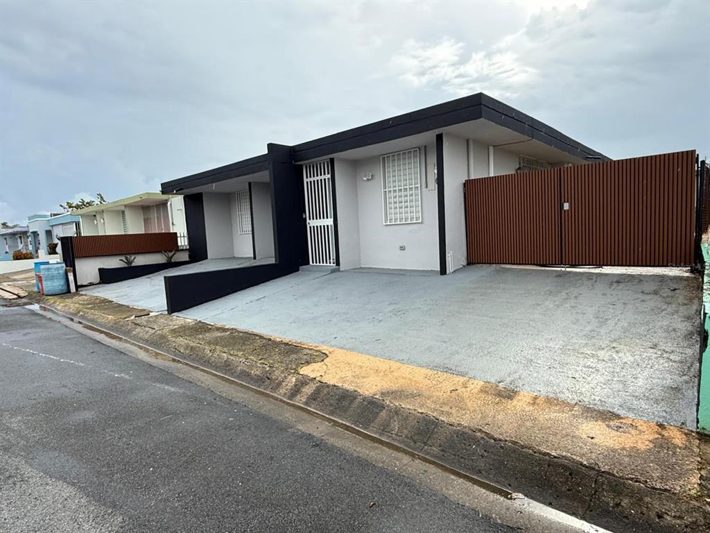 A single-story house with a flat roof, gray concrete driveway, and a brown privacy fence — VILLA CAROLINA CALLE 102 UNIT 106-19, CAROLINA, PR