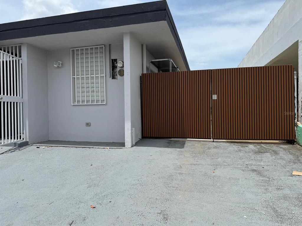 A gray exterior wall with a window security grate and a large brown slatted gate — VILLA CAROLINA CALLE 102 UNIT 106-19, CAROLINA, PR
