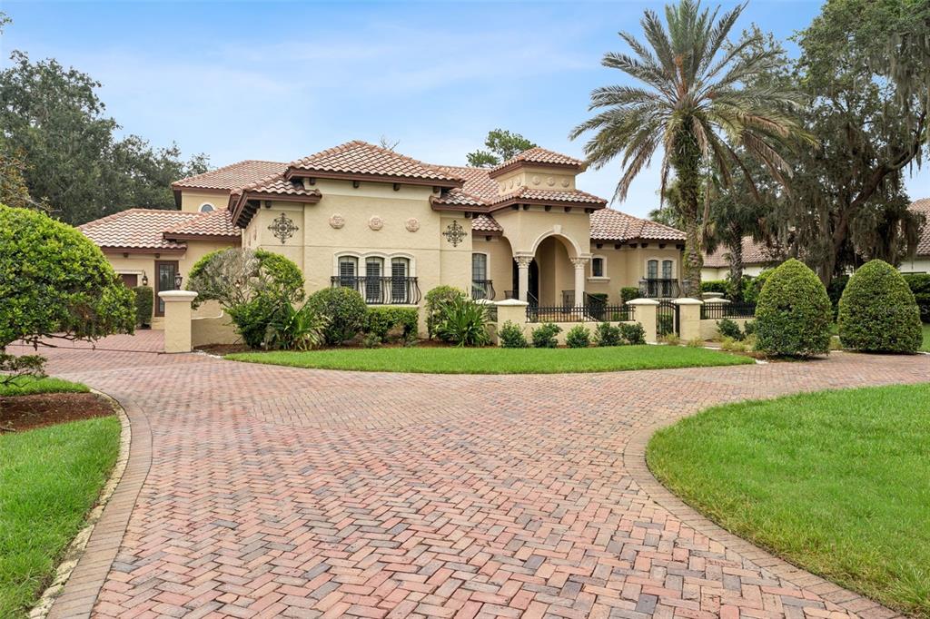 A tan stucco house with a tiled roof and a large brick-paved driveway — 7764 ISLEWOOD COURT, SANFORD, FL