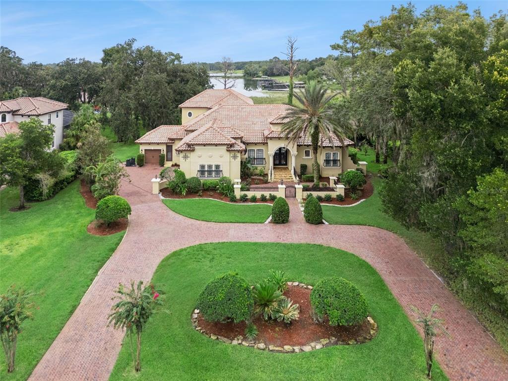 An aerial view of a Mediterranean-style house with a circular brick driveway and a lake view — 7764 ISLEWOOD COURT, SANFORD, FL