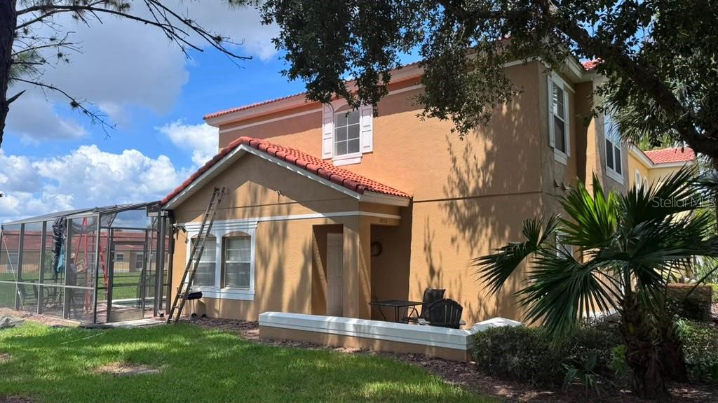 A two-story stucco house with a screened-in pool enclosure and a small patio area — 3050 SECRET LAKE DRIVE, KISSIMMEE, FL