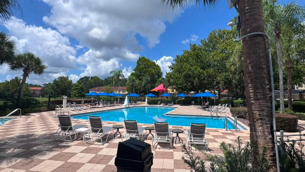 A swimming pool with lounge chairs and blue umbrellas on a paved patio — 3050 SECRET LAKE DRIVE, KISSIMMEE, FL
