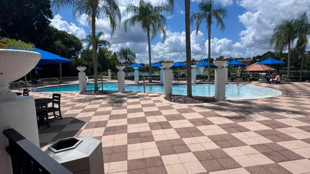 A swimming pool with a checkered patio, palm trees, and blue umbrellas on a sunny day — 3050 SECRET LAKE DRIVE, KISSIMMEE, FL