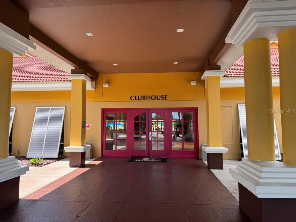 The exterior entrance of a clubhouse features yellow walls, red double doors, and white columns — 3050 SECRET LAKE DRIVE, KISSIMMEE, FL