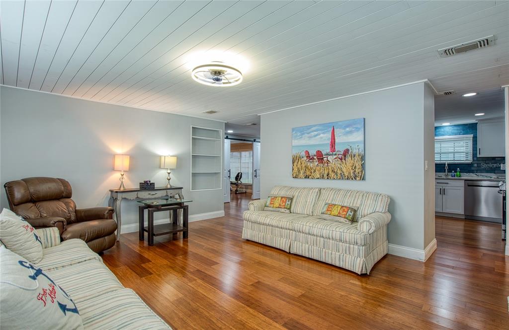 A living room features wood flooring, a white plank ceiling, and a striped sofa — 407 DOLPHIN DRIVE S, OLDSMAR, FL
