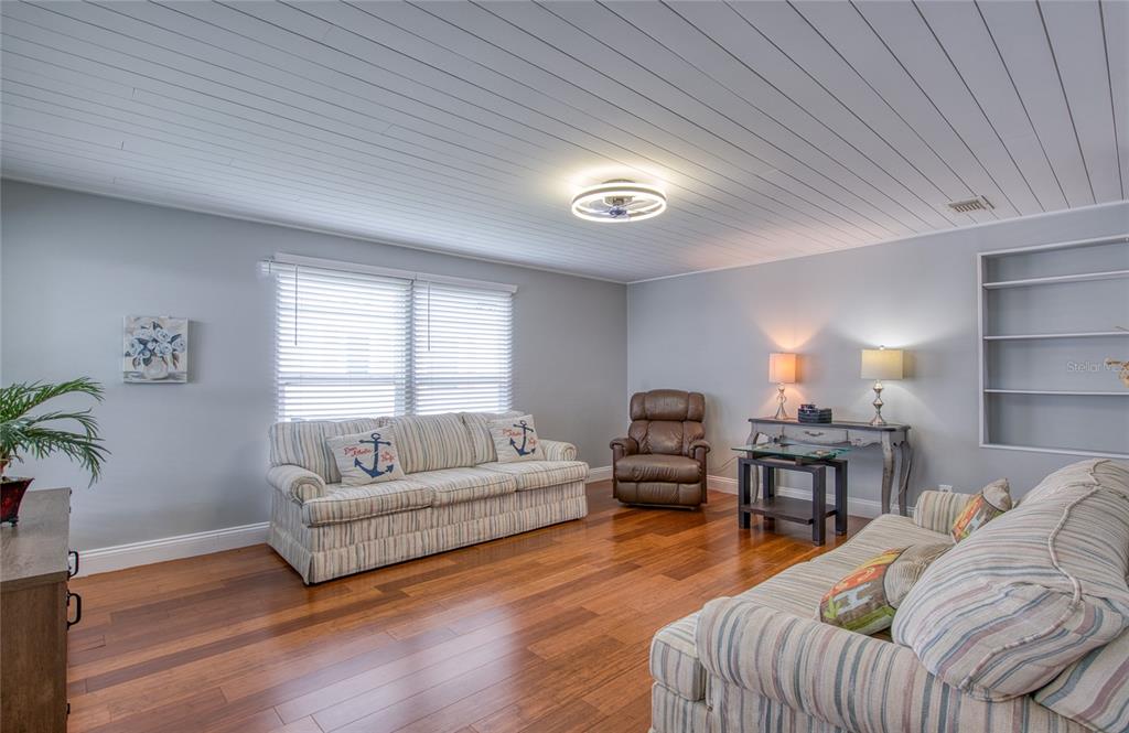 A living room features light gray walls, a plank ceiling, and hardwood flooring — 407 DOLPHIN DRIVE S, OLDSMAR, FL