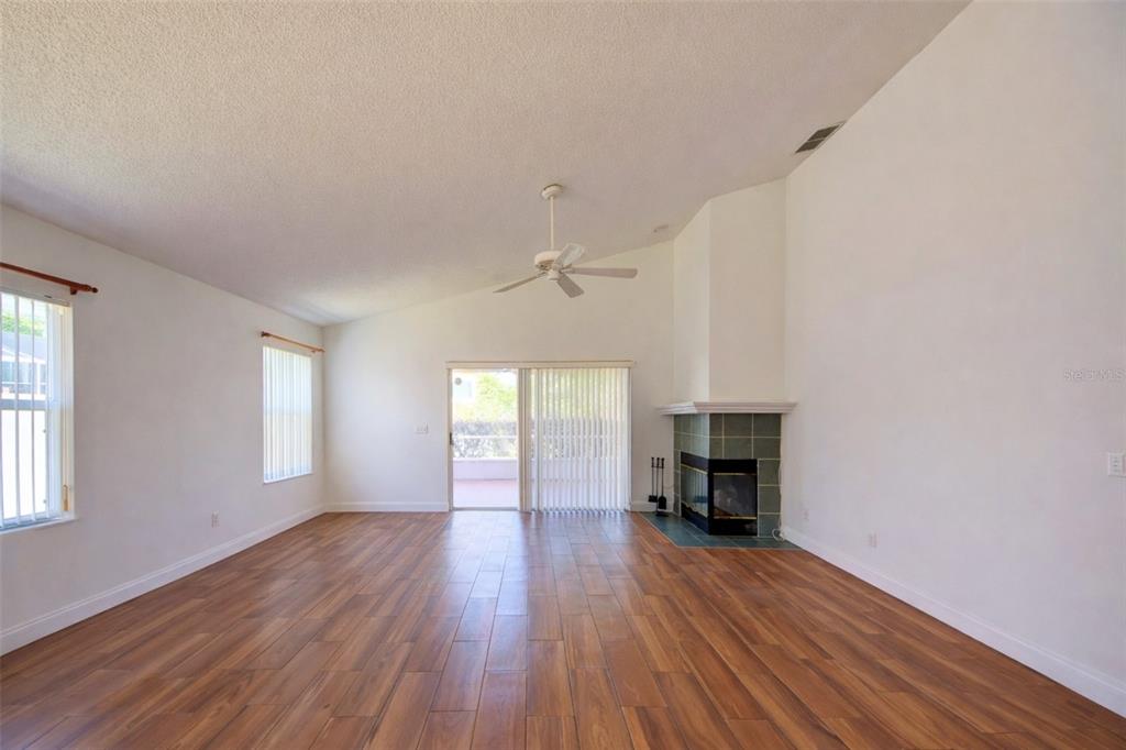 A living room with wood-look tile flooring, a fireplace, a ceiling fan, and sliding doors — 635 ROCHESTER LOOP, DAVENPORT, FL