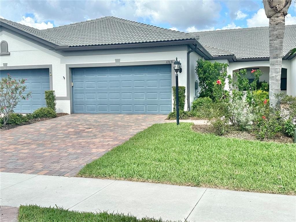 A single-story house with a blue garage door, paver driveway, and landscaped front yard — 17631 CAMDEN DRIVE, BRADENTON, FL