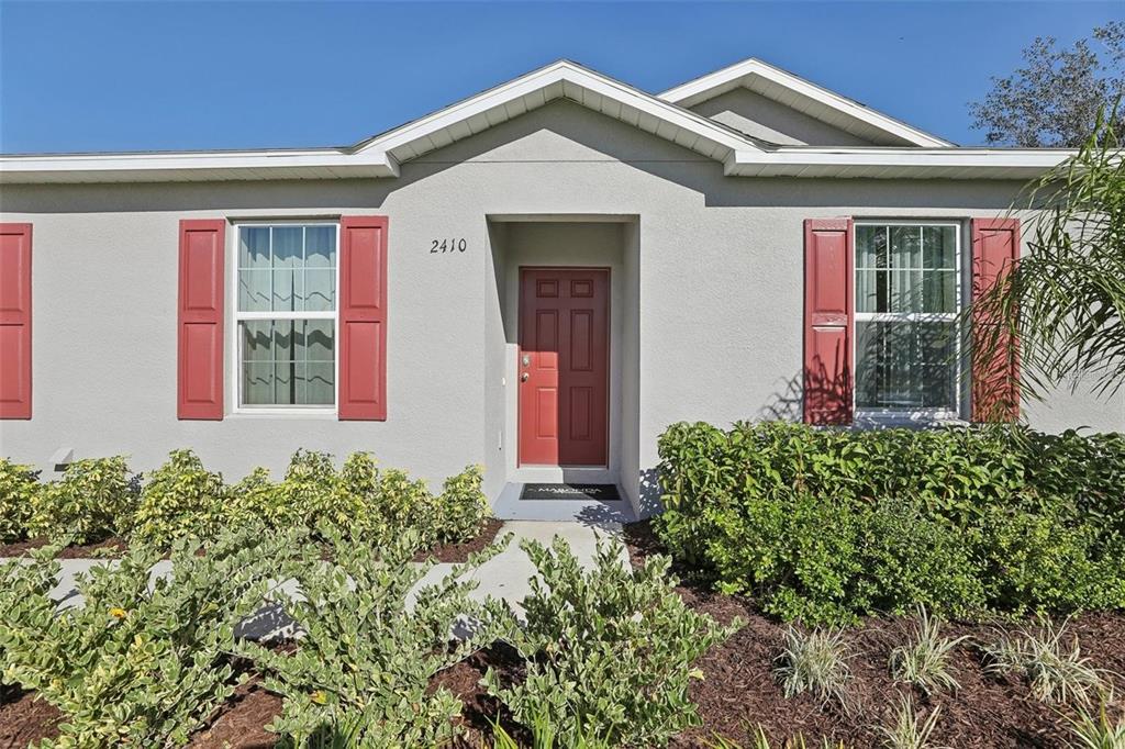 The exterior of a single-story house features a red front door and matching window shutters — 2410 PARK AVENUE, INDIAN LAKE ESTATES, FL