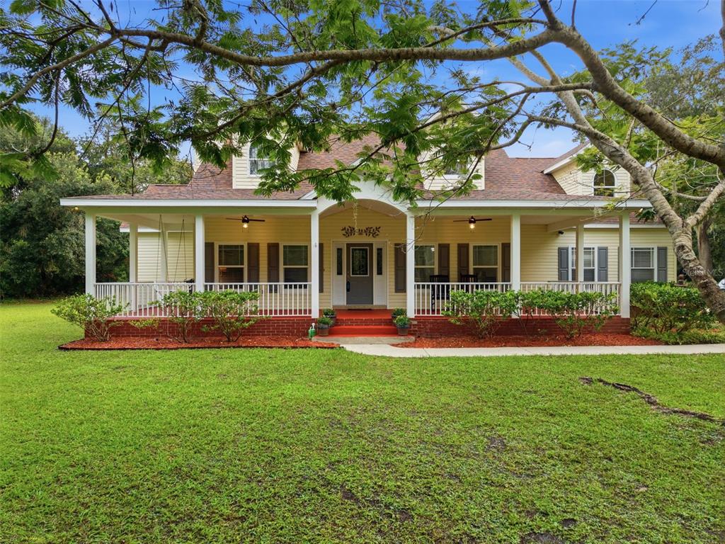 A two-story yellow house with a large covered front porch and a spacious green lawn — 3407 FLAGSTAFF CIRCLE, WIMAUMA, FL