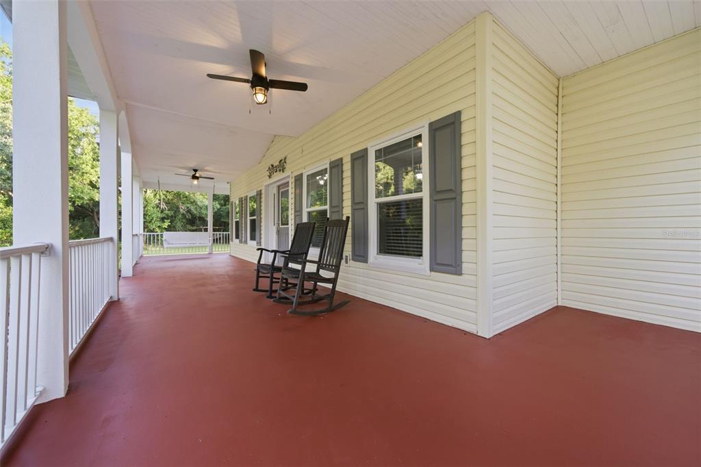 A covered porch with a red floor, two rocking chairs, and a hanging swing — 3407 FLAGSTAFF CIRCLE, WIMAUMA, FL