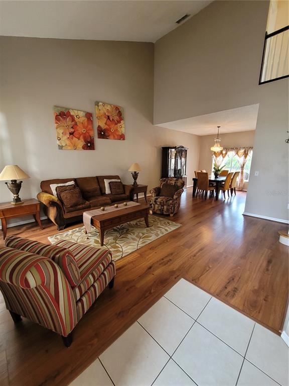 A living room with wood flooring, a vaulted ceiling, and an adjacent dining area — 27640 BREAKERS DRIVE, WESLEY CHAPEL, FL
