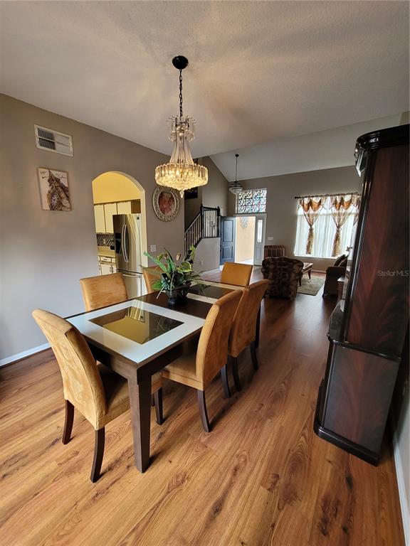 A dining room with a glass-topped table, upholstered chairs, and wood flooring — 27640 BREAKERS DRIVE, WESLEY CHAPEL, FL
