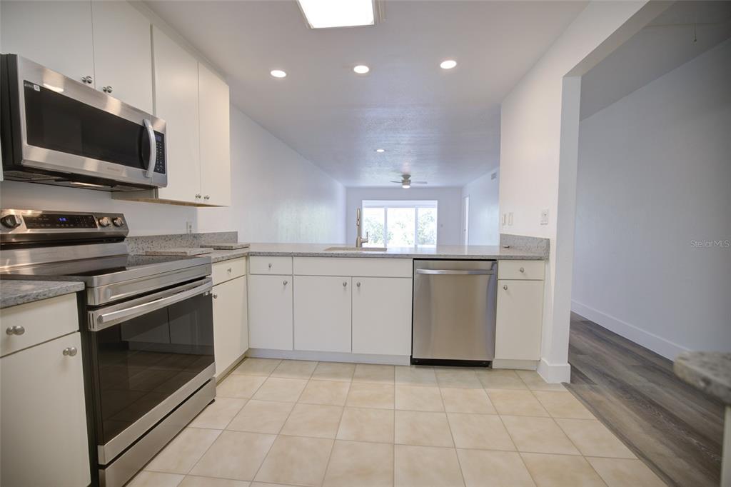 A kitchen features white cabinets, stainless steel appliances, granite countertops, and light-colored tile flooring — 10134 REGAL DRIVE UNIT 1, LARGO, FL