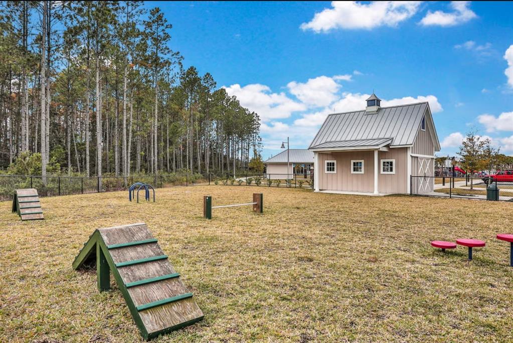 A fenced dog park features agility equipment, a small barn-style building, and surrounding pine trees — 162 FERN VALLEY COURT, ST AUGUSTINE, FL