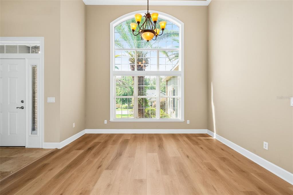A dining room with light wood floors, a large arched window, and a hanging chandelier — 7560 WHITE OAKS ROAD, ALACHUA, FL