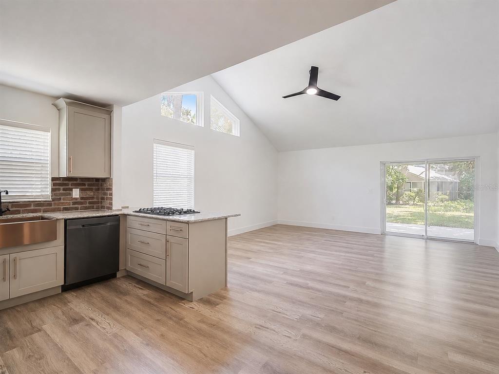 A kitchen with light-colored cabinets and a brick backsplash opens into a vaulted-ceiling living area — 4956 VILLAGE GARDENS DRIVE UNIT 145, SARASOTA, FL