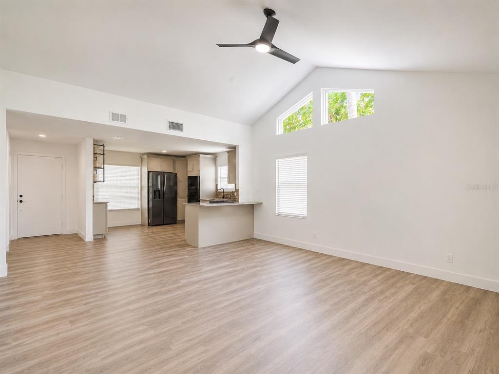 An open-concept living area features light wood-look flooring, a kitchen island, and vaulted ceilings — 4956 VILLAGE GARDENS DRIVE UNIT 145, SARASOTA, FL