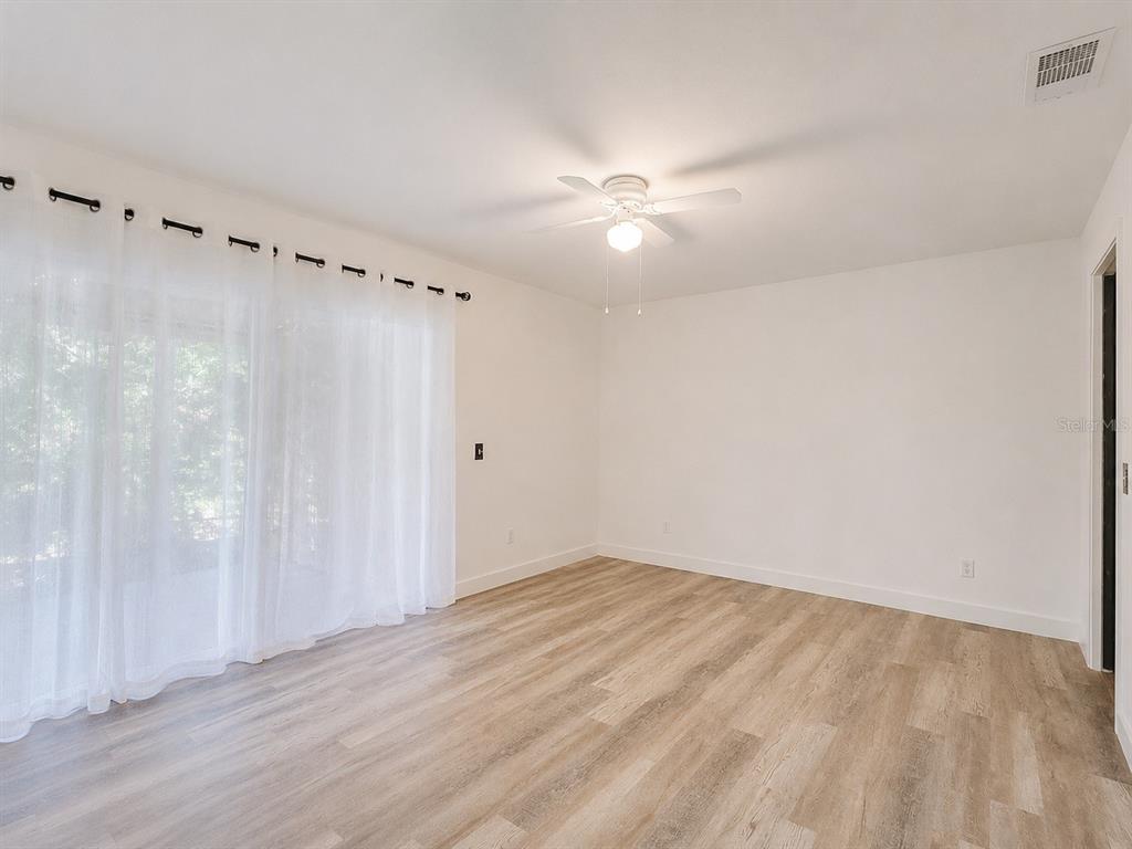 An empty room with light wood-look flooring, white walls, a ceiling fan, and sheer curtains — 4956 VILLAGE GARDENS DRIVE UNIT 145, SARASOTA, FL
