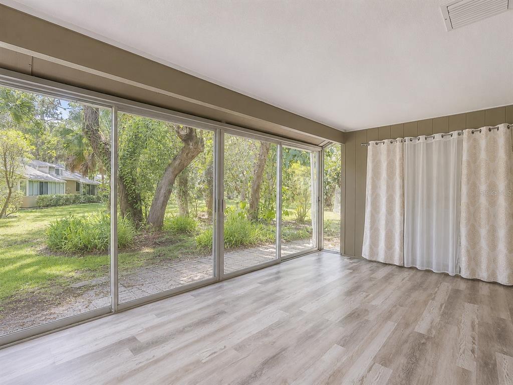 A sunroom features light wood-look flooring, large sliding glass doors, and views of a wooded yard — 4956 VILLAGE GARDENS DRIVE UNIT 145, SARASOTA, FL