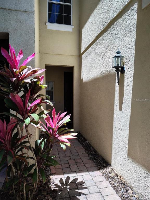 A paved walkway leads to a recessed entryway beside a wall with a mounted light fixture — 6043 STRADA ISLE WAY, ORLANDO, FL