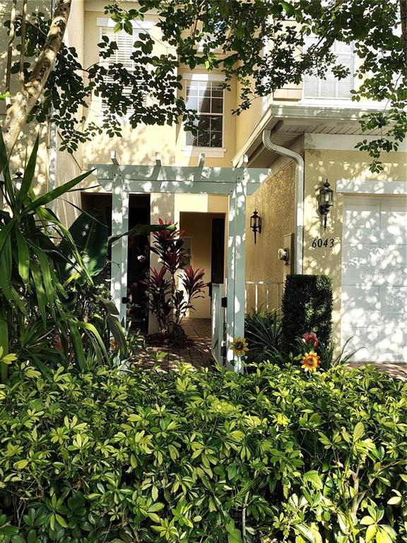 A beige two-story townhouse features a white pergola over the entrance and a garage — 6043 STRADA ISLE WAY, ORLANDO, FL