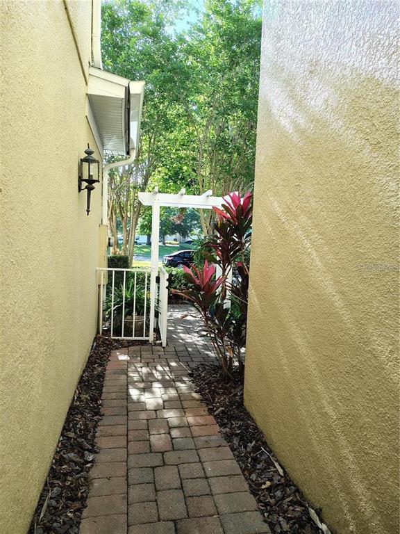 A paved walkway leads between two stucco walls toward a white arbor and gate — 6043 STRADA ISLE WAY, ORLANDO, FL