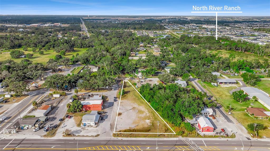 An aerial view shows a triangular vacant lot situated between commercial buildings and trees — 12346 US-301, PARRISH, FL