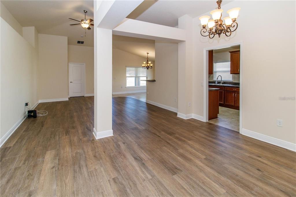 An open-concept living and dining area features wood-look flooring, neutral walls, and two chandeliers — 13541 NITI DRIVE, HUDSON, FL