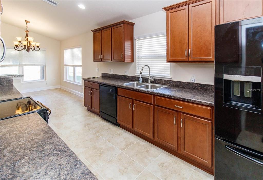 A kitchen with wood cabinets, dark countertops, black appliances, and light tile flooring — 13541 NITI DRIVE, HUDSON, FL