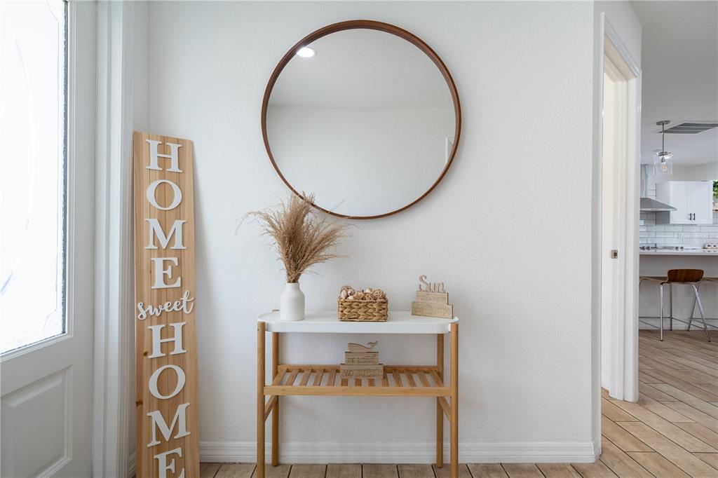 A bright entryway features a round mirror, a wooden console table, and a vertical sign — 7354 BILTMORE DRIVE, SARASOTA, FL