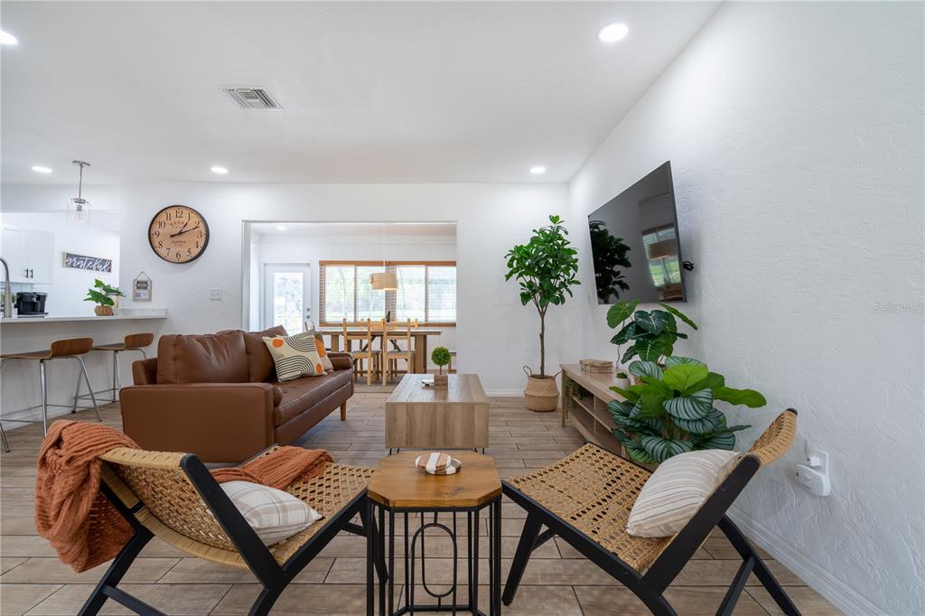 A living room features a brown leather sofa, two woven chairs, and a wall-mounted television — 7354 BILTMORE DRIVE, SARASOTA, FL