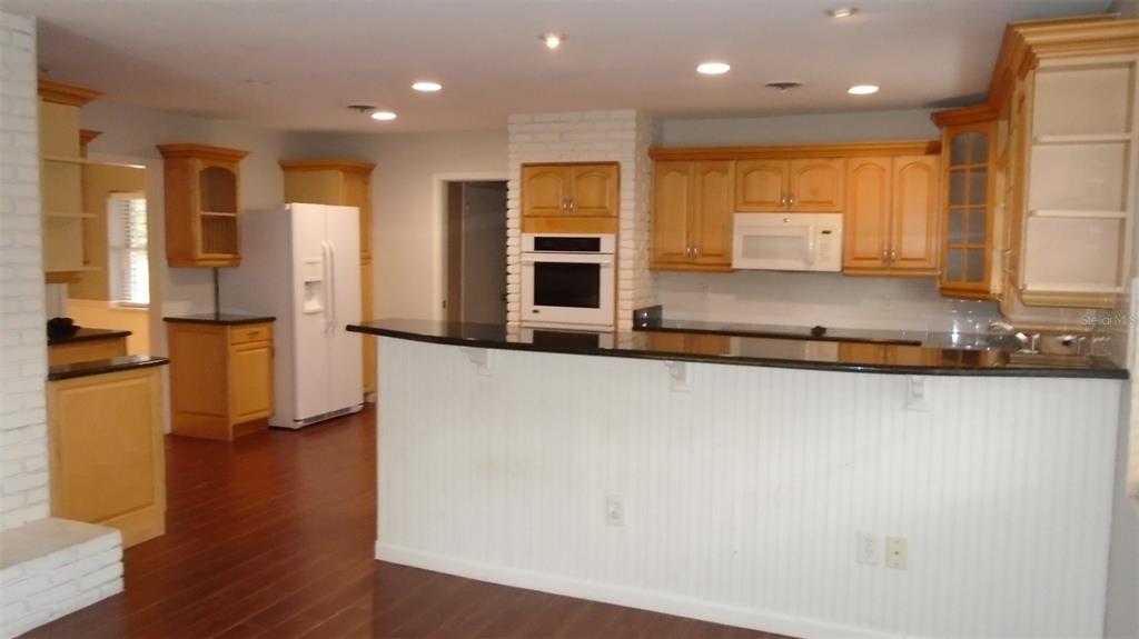 A kitchen features wood cabinets, a white refrigerator, a black countertop, and white brick accents — 2330 MOHAWK TRAIL, MAITLAND, FL