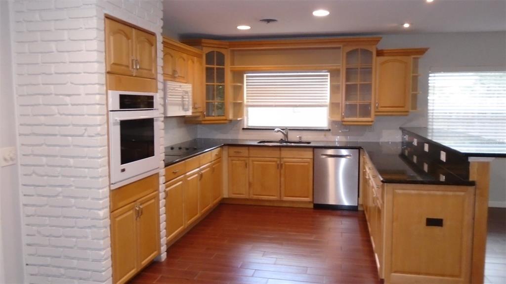 A kitchen features light wood cabinets, black countertops, stainless steel appliances, and a white brick wall — 2330 MOHAWK TRAIL, MAITLAND, FL