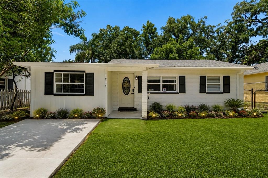 A single-story white house with black shutters and a concrete driveway sits on a lawn — 1614 E MAPLE AVENUE, TAMPA, FL
