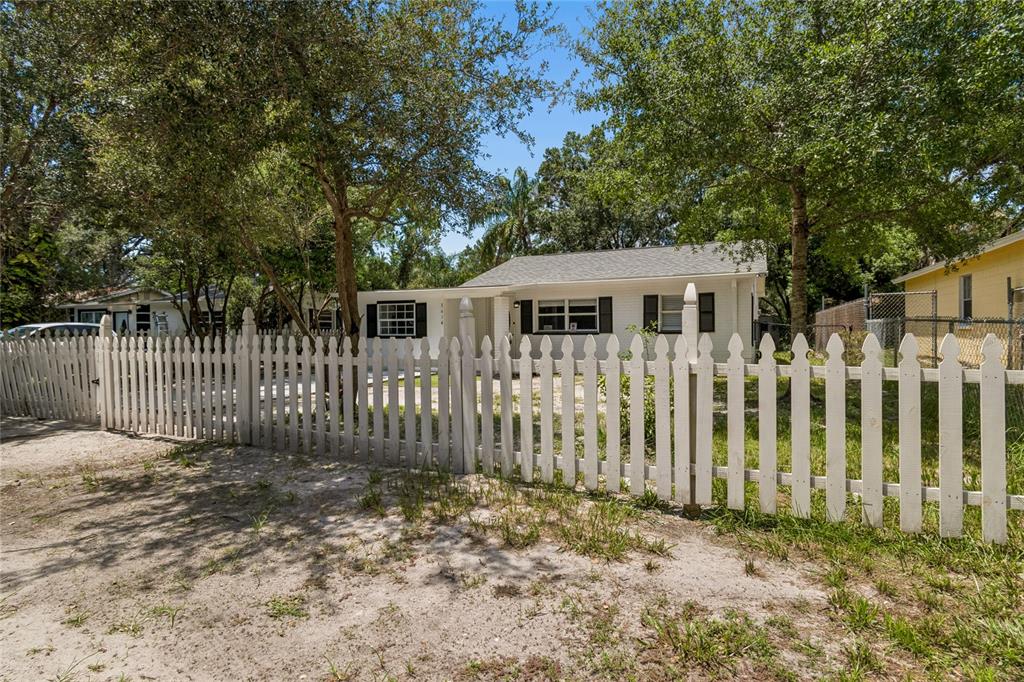 A white house with black shutters sits behind a white picket fence under large trees — 1614 E MAPLE AVENUE, TAMPA, FL