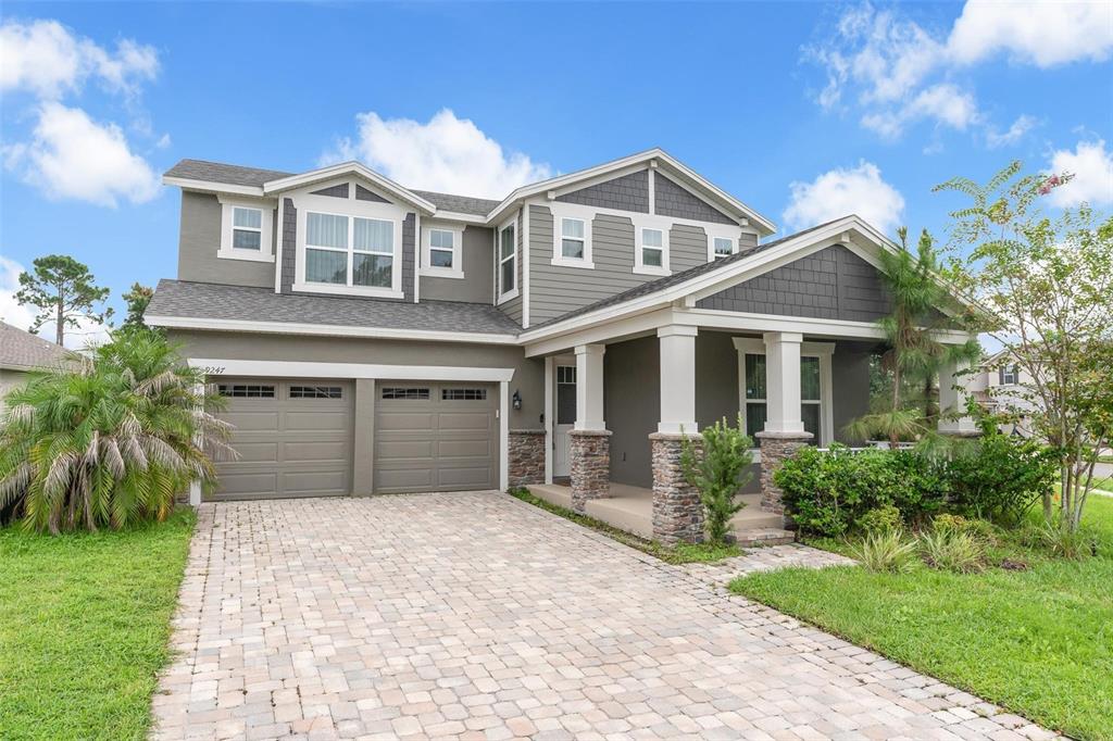 A two-story house with a stone-accented porch, gray siding, and a paved driveway — 9247 LEGADO DRIVE, WINTER GARDEN, FL