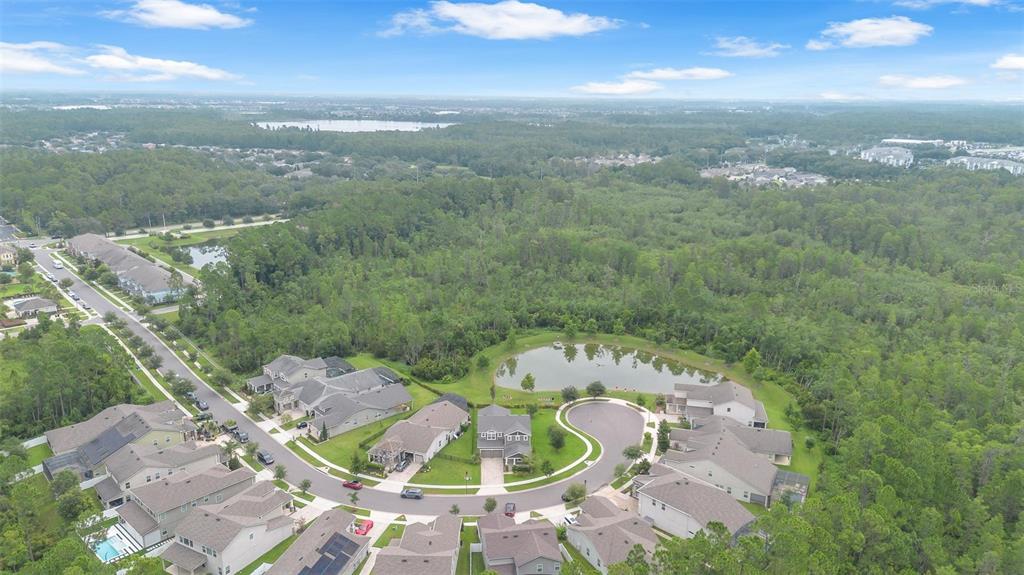 An aerial view shows a suburban neighborhood with houses surrounding a small pond and forest — 9247 LEGADO DRIVE, WINTER GARDEN, FL