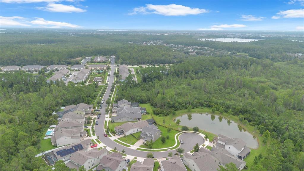 An aerial view shows a suburban neighborhood with houses, a pond, and surrounding forest — 9247 LEGADO DRIVE, WINTER GARDEN, FL
