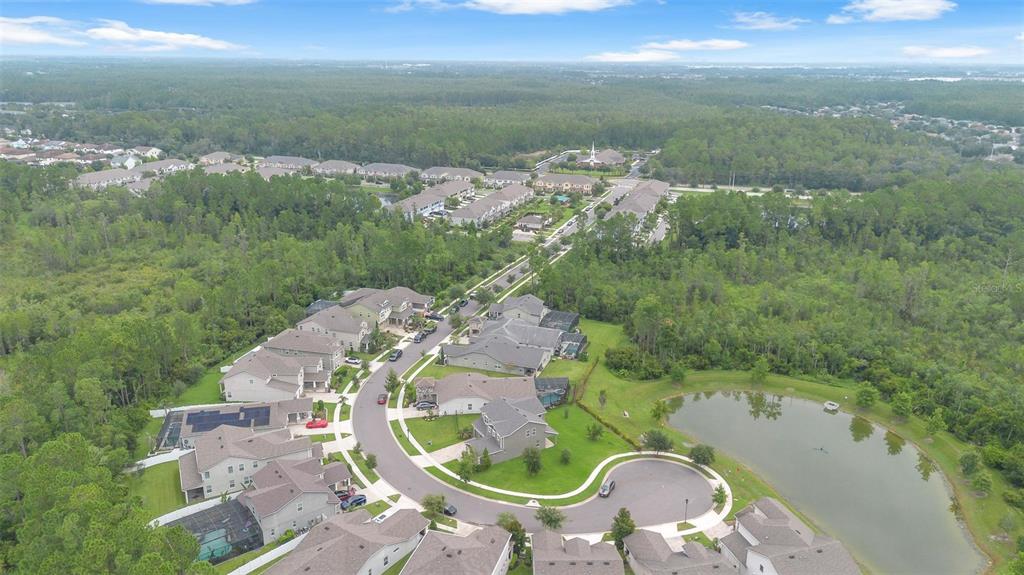 An aerial view shows a suburban neighborhood with houses, a pond, and surrounding forest — 9247 LEGADO DRIVE, WINTER GARDEN, FL